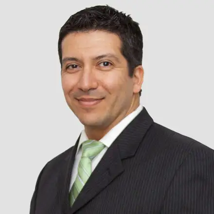 A man in a dark suit, white shirt, and light green striped tie poses against a plain light background, smiling slightly—like he just passed his Eye Exam at an Ashburn VA Optometrist.