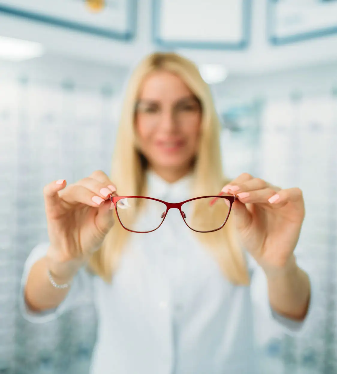 A woman holds red eyeglasses toward the camera in an optical store, with the background softly blurred—an inviting scene at your trusted Ashburn VA Optometrist, perfect for your next eye exam.